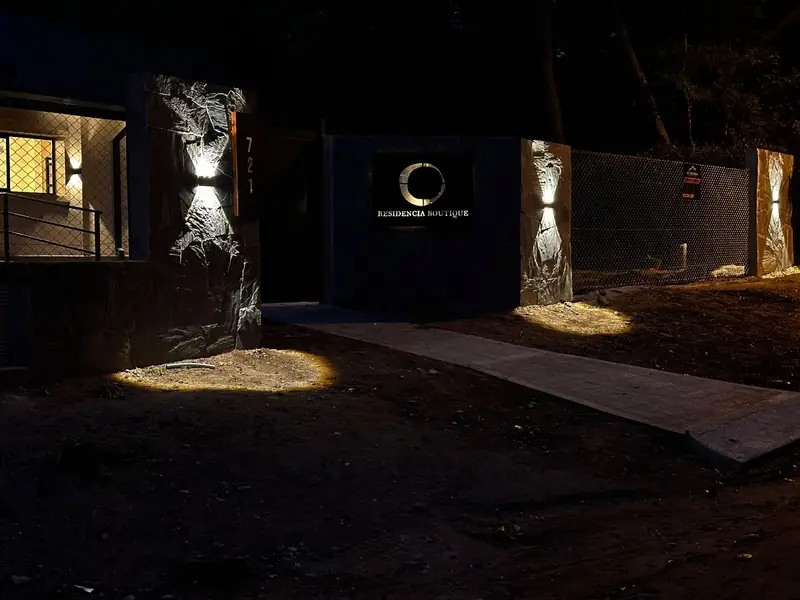 Ingreso de Haus Leben de noche, con muros de piedra iluminados y el cartel de Residencia Boutique